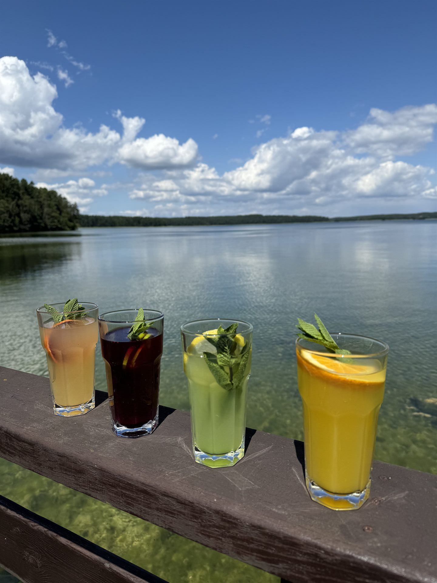 kolorowe drinki ułożone obok siebie na poręczy pomostu
